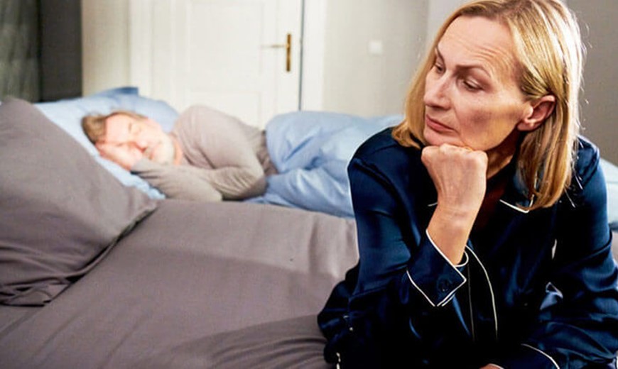 Frau sitzt an der Bettkante Jetlag trifft Frauen stärker