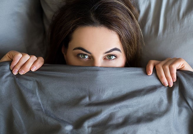 Frau unter der Bettdecke Innere Unruhe und Schlafstörungen treten häufig gemeinsam auf
