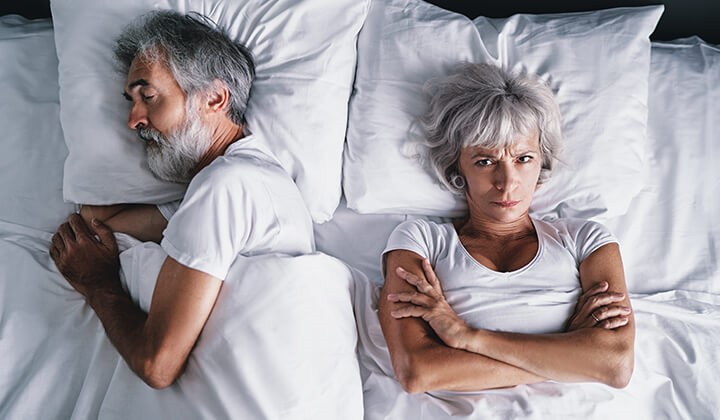 Genervte Frau liegt neben schlafendem Mann Schlafstörungen im Alter sind keine Seltenheit